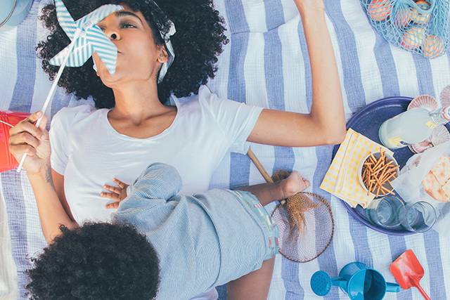 Mother blowing on a pinwheel while laying on a blanket with her baby boy